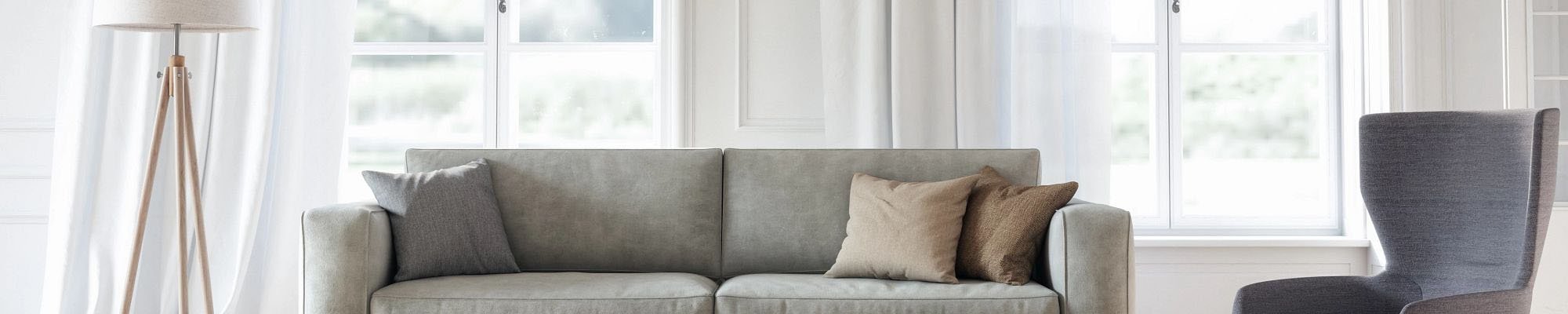 Bright living room with a gray couch, large windows with white drapes and a large gray area rug on hardwood flooring from Triangle Flooring Center in Carrboro, North Carolina