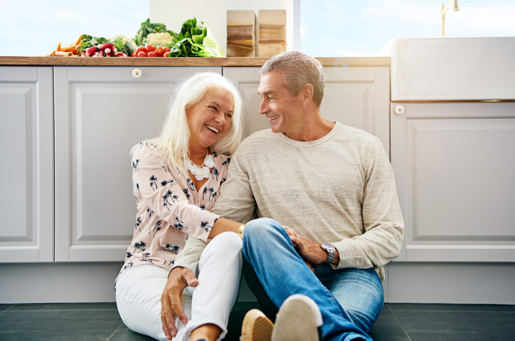 Two elderly people sitting on a kitchen floor sharing a moment together